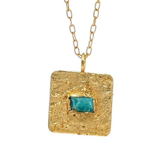 Gold necklace with a square pendant featuring an emerald in the middle